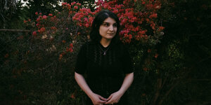 Porträt der Musikerin Sarah Davachi, die vor einer Rosenhecke steht