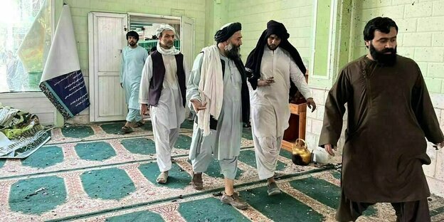 fünf Afghanen gehen über einen mit Glassplittern übersäten Teppich in einer Moschee