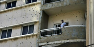 Ein Mann steht auf dem Balkon in Beirut. Die Häuserfront zeigt zahlreiche Einschußlöcher