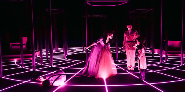 Das pink angestrahlte Ensemble vor schwarzem Hintergrund mit einem kreisförmigen pinken Netzmuster auf dem Boden.
