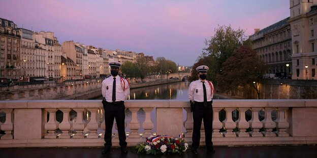 Polizisten stehen neben einem Blumenkranz auf der Saint-Michel-Brücke in Paris