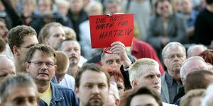 Eine Menschenmenge demonstriert, ein mann hällt ein rotes Schild mit der Aufschrift "Die Rote Karte Für Hartz IV"