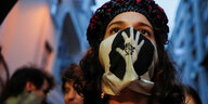 Eine Frau trägt einen Mundschutz, auf den eine Hand aufgedruckt ist und die Aufschrift "Free SzFE"
