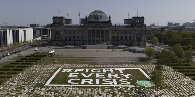 Protestschilder und der Spruch "fight every crisis" auf der Wiese vor dem Reichstag