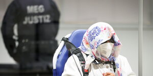 Irmgard Furchner hat ihr Gesicht mit kopftuch und maske verdeckt, sie sitzt angeschnallt in einem Rollstuhl
