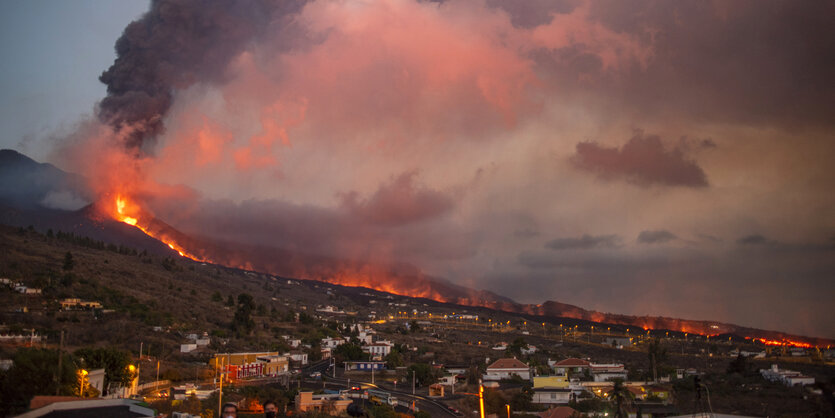 Lavaströme fliessen den Berg hinuter, rote Rauch- und Aschewolken im Vordergrund die Stadt Los Llanos