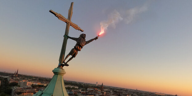 Figur hängt an Kreuz auf Kirche, in der Hand eine brennende Fackel