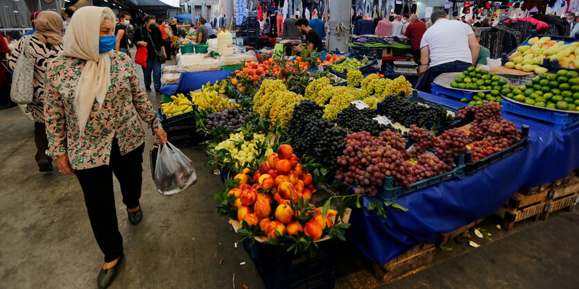 Pfirsiche und Trauben und ander Obstsorten, schön aufbereitet auf einem markstand, davor eine Frau mit Einkaufstüte