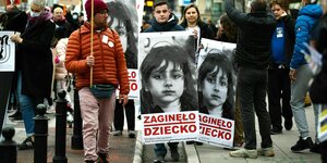 Protestirende tragen zwei große Plakate mit dem Foto eines kleinen Mädchens