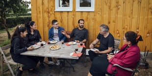 6 Menschen sitzen um einen Tisch im Garten