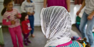 Frau mit weißem Kopftuch schaut auf spielende Kinder