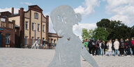 Die Metallsilhouette eines Mädchens vor einem alten Bahnhof, im Hintergrund eine Schulklasse