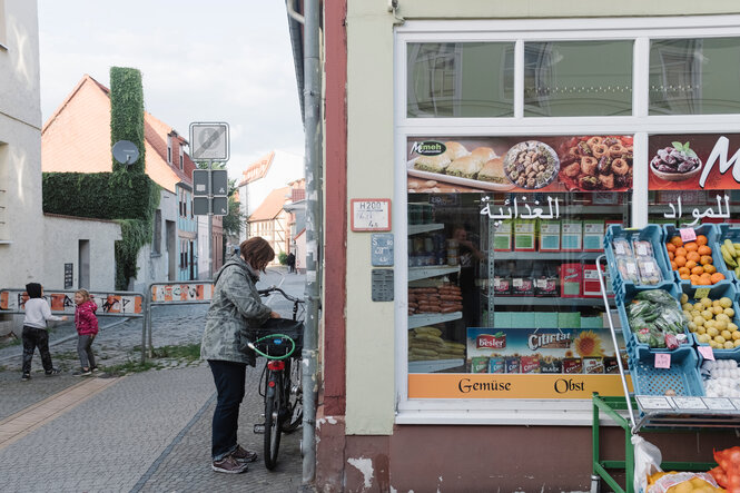 Neben einem Lebensmittelladen in einer Kleinstadt schließt eine Frau ihr Fahrrad auf