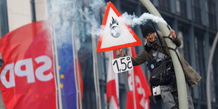 Ein Protestler ist eine Laterne hochgeklettert, dahinter eine Fahne der SPD