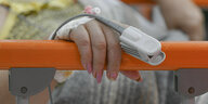 Eine Hand hält sich an einem krankenhausbett fest, die Frau hat rosa Fingernägel