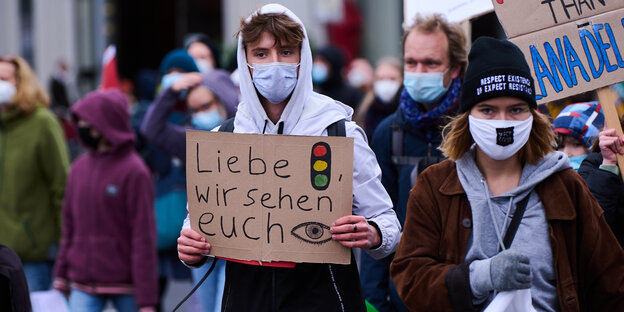 Zwei junge Menschen im Vordergrund einer Demo mit Schild "Liebe Ampel, wir sehen euch".