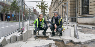 Zwei Frauen in Arbeitskleidung vor aufgebrochenem Pflaster