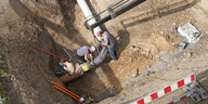 Zwei Personen arbeiten in einer Grube an einem Rohr.
