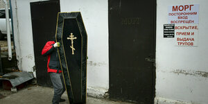 Ein Mann trägt einen goldverziehrten Sarg zur Leichenhalle
