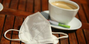 Eine FFP2-Maske liegt neben einer Tasse Kaffee auf einem Tisch