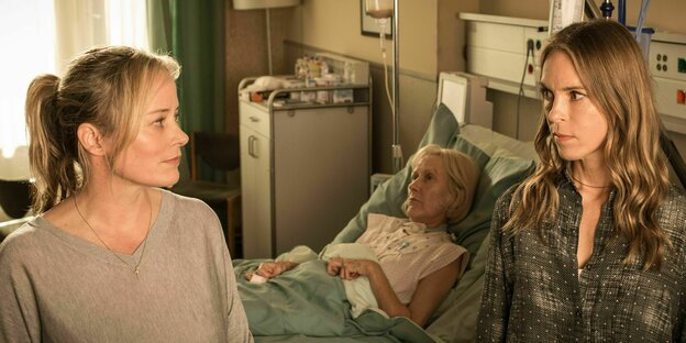 Filmszene, eine alte Frau liegt regungslos in einem Krankenhausbett, im Vordergrund zwei Frauen, gespielt von Silke Bodenbender und Anneke Kim Sarnau