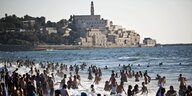 Menschemenge badet im Meer vor der Stadt Jaffa im Hintergrund.