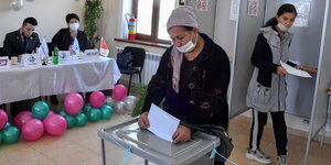 Frau mit Mund-Nasenschutz wirft einen Wahlzettel in die Urne
