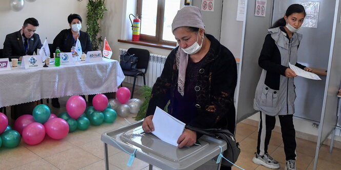 Frau mit Mund-Nasenschutz wirft einen Wahlzettel in die Urne