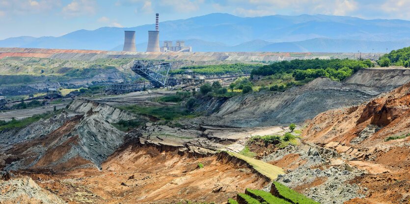 Ausgebaggerte Landschaft mit Braunkohke, ein Schaufelbagger, ein Kraftwerk und Berge