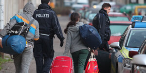 Zwei Polizisten eskortieren zwei junge Menschen mit Gepäck