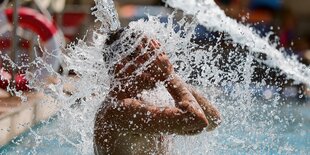 Eine Person ohne Oberbekleidung lässt sich in einem Schwimmbecken Wasser auf den Kopf spritzen.