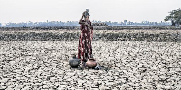 Eine Frau steht auf einem vertrockneten Boden und schüttet sich Wasser ins Gesicht.