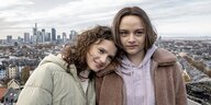 Zwei junge Frauen stehen auf einem Dach: Die Skyline von Frankfurt im Hintergrund