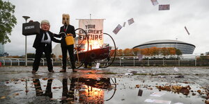 Aktivisten verkleidet als Boris Johnson , daneben ein Mann mit Ölkanister auf dem Kopf und in der Hand