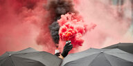 Rote Rauchfahnen, eine Hand mit Handschu und Regenschirme