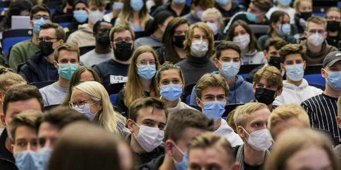 Eng zusammen sitzende junge Menschen mit Masken