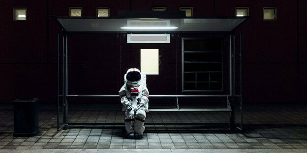 Ein Astronaut sitzt nachts an einer Bushaltestelle