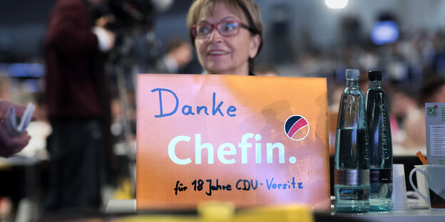 Danke chefin für 18 jahre CDU-Vorsitz steht auf einem orangen Schild, dahinter ein Frauenkopf unscharf