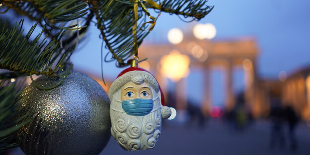 Eine Weihnachtskugel in Form eines Weihnachtsmanns mit Maske hängt vor dem Brandenburger Tor