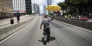 Ein Mann mit einem gelben Regenschirm läuft auf einer Straße in HongKong