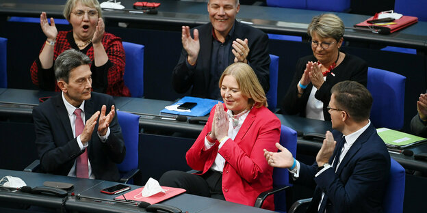 Eine Frau sitzt im Bundestag und wird von den Umsitzenden beklatscht