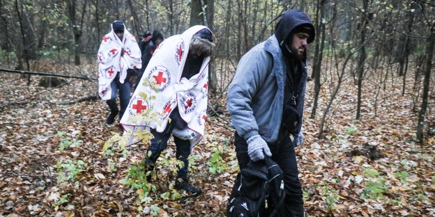 Außerhalb des polnischen Notstandsgebiets an der Grenze zu Belarus entdeckten Ärzte fünf Geflüchtete. Sie sind in Decken des roten Kreuzes gehüllt und werde durch einen Wald geführtd helfen ihnen