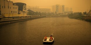 Ein Paar im Tretboot in Jakutsk. Über der sibirischen Stadt hängt gelber Qualm von nahegelenen Waldbränden