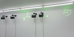 Unter der Decke der Future Gallery hängen vier Lasermaschinen, die abstrakte Linien in neongrüner Leuchtschrift an die Wand projizieren