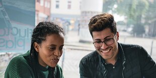 Eine junge Frau und ein junger Mann schauen gut gelaunt auf einen Laptop-Bildschirm.