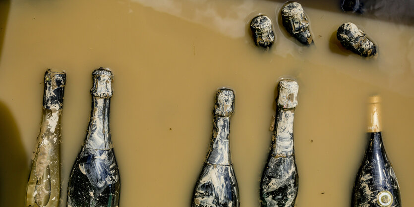 Sekt- und Weinflaschen, halb verdeckt von einer dreckigen Wasserbrühe