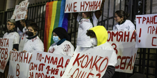 Schilder mit roter Schrift werden gehalten von Demonstranten mti Masken