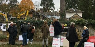 Vor einem verwahrlosten Haus stehen Protestler:innen