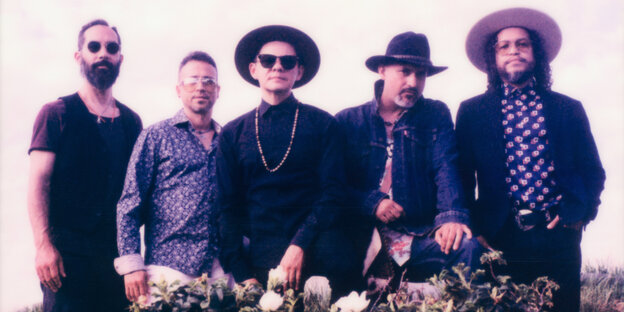Ddie fünf Mitglieder der Band Dos Santos aus Chicago stehen in weißer Kleidung vor einem dunklen Hintergrund in einem Fotostudio