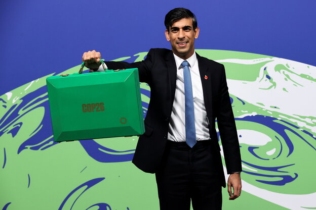 Der britische Finanzminister Rishi Sunak hält vor der Abbildung der Erdkugel einen grünen Koffer hoch
